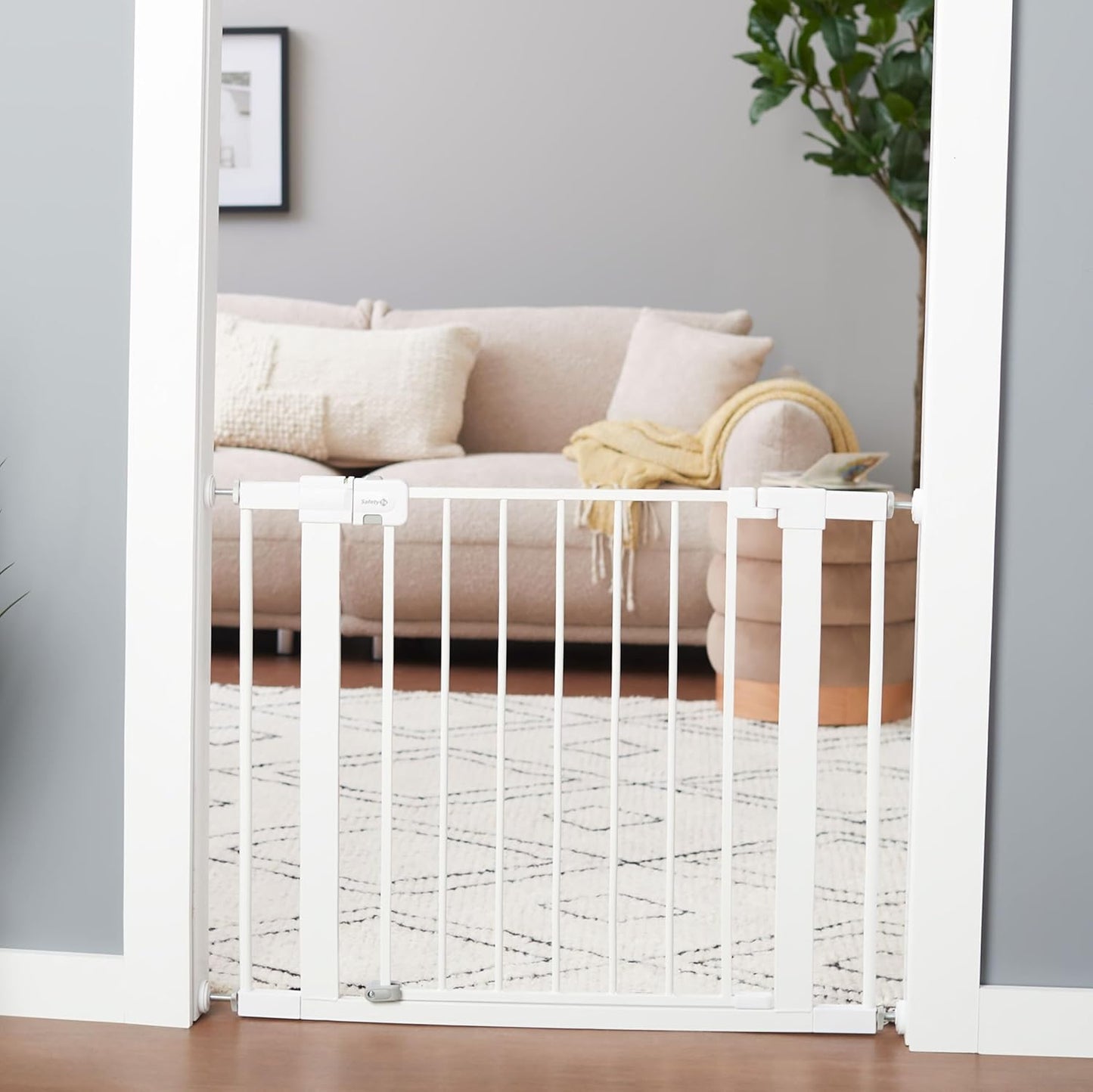 White baby gate in a living room with a couch and plant.